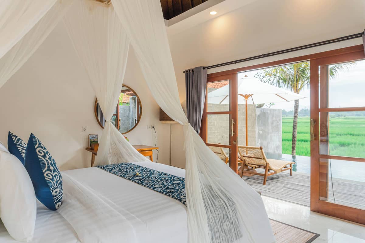 A bedroom with a canopy bed, a view of a palm tree, and a wooden deck.