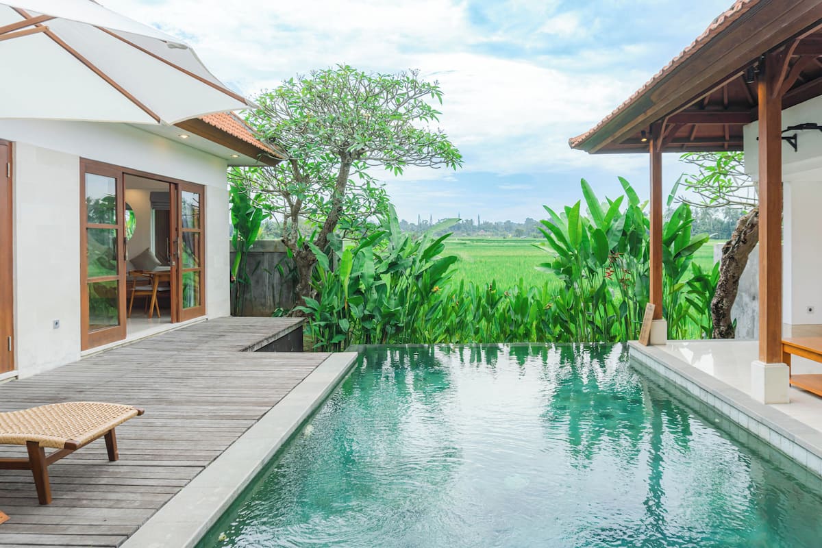A swimming pool with a wooden deck and a view of a green field.