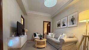 Un salon avec un canapé, une table basse, un téléviseur et des œuvres d’art encadrées accrochées au mur.