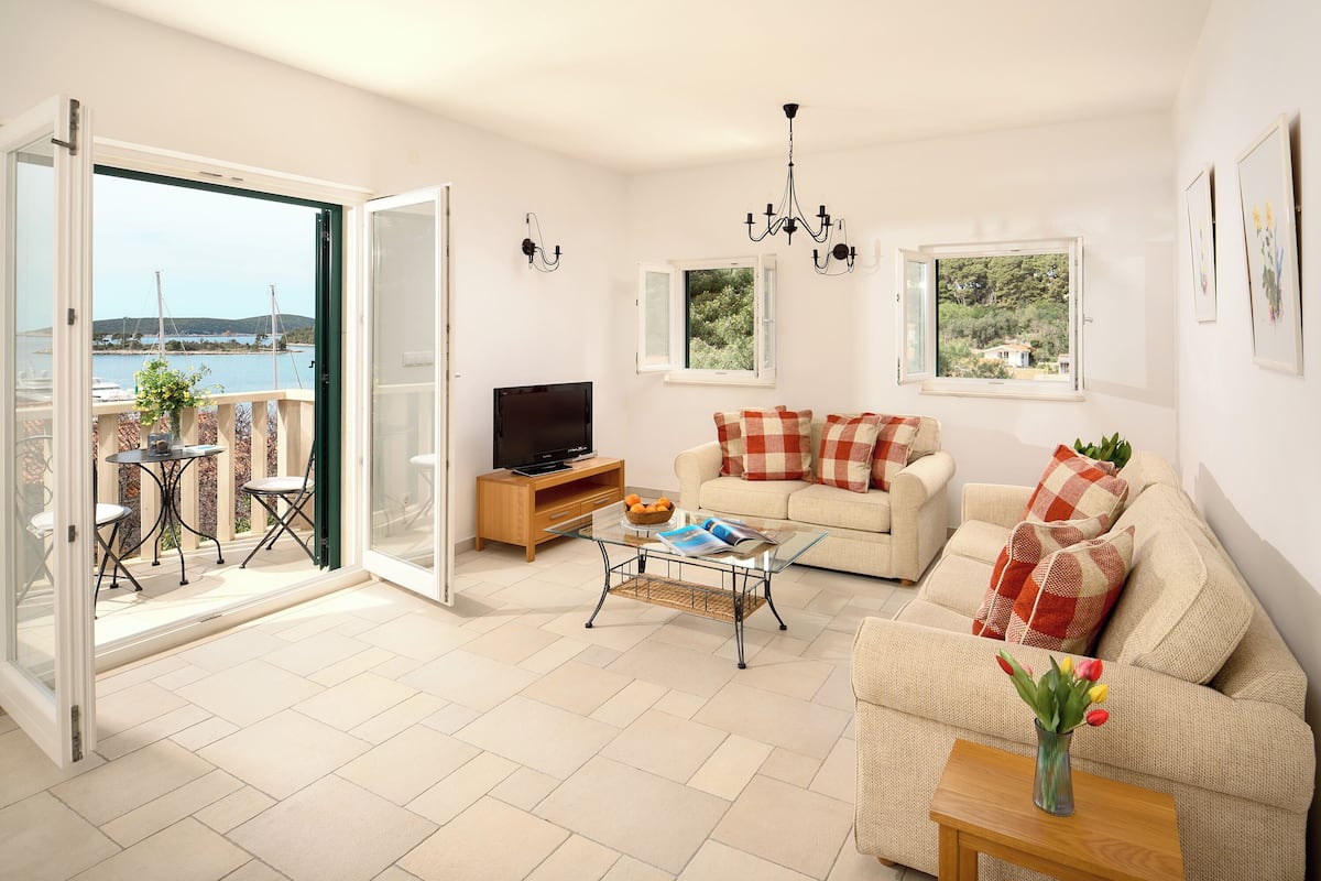 Een woonkamer met een bank, salontafel, tv-meubel en een balkon met uitzicht op zee.