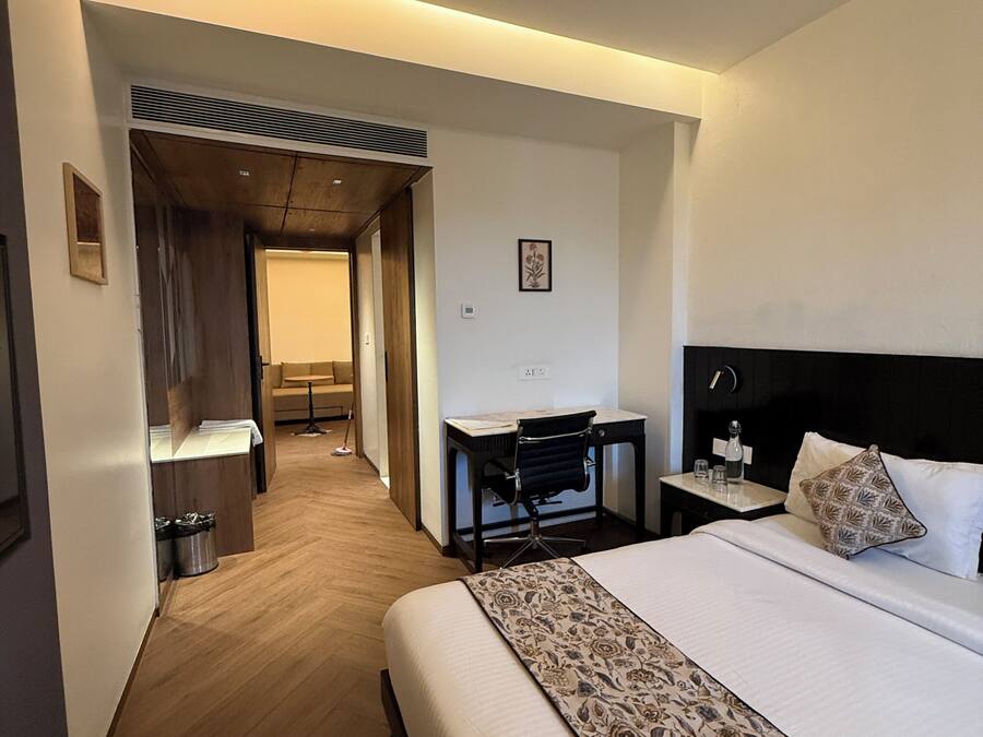 Ein Hotelzimmer mit einem großen Bett, einem Schreibtisch und einem Stuhl. Ein kleiner Tisch beherbergt eine Lampe, und an der Wand hängt ein Bild.