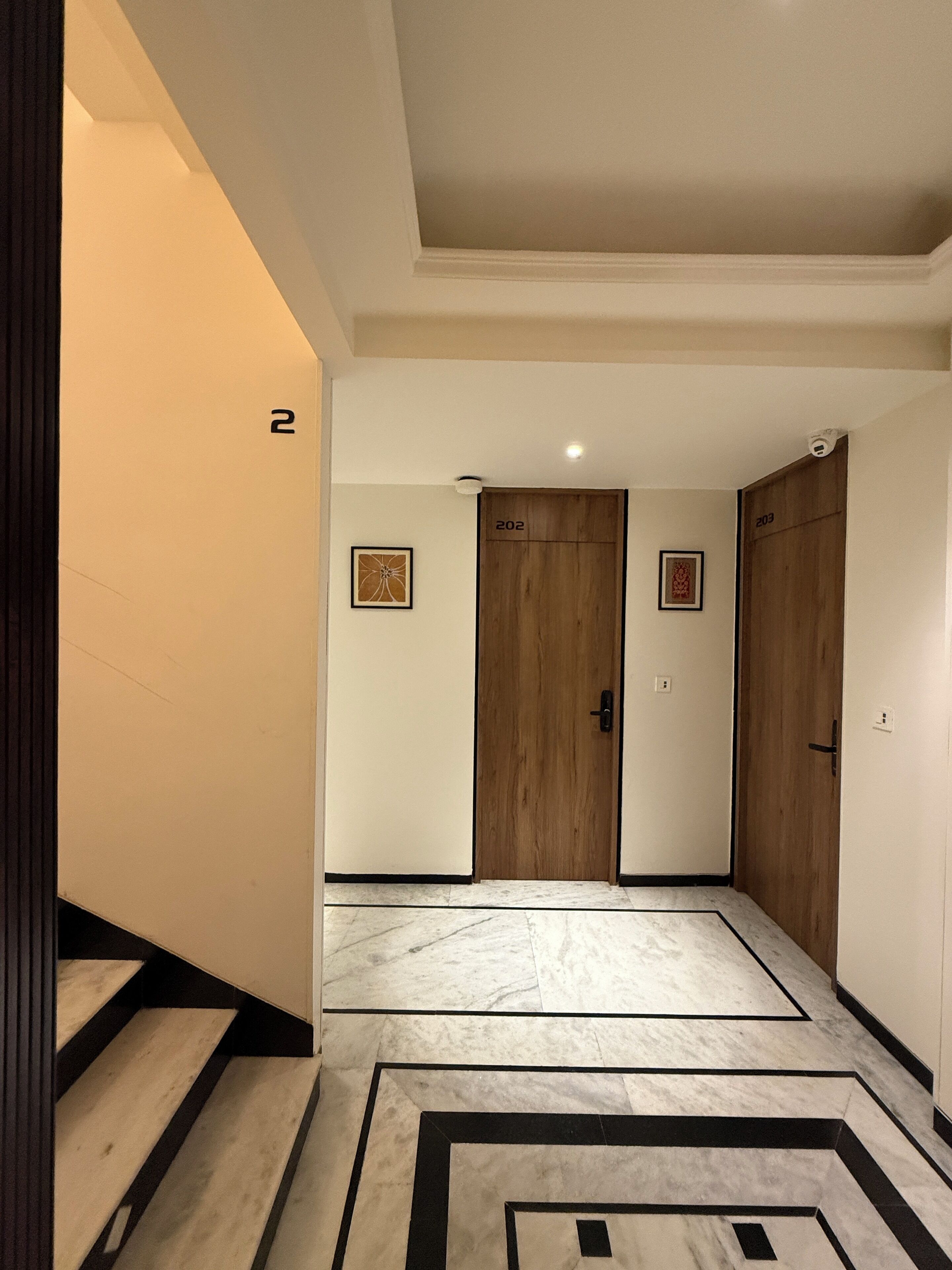 A hallway with a marble floor, wooden doors numbered 202 and 203, and a staircase on the left.
