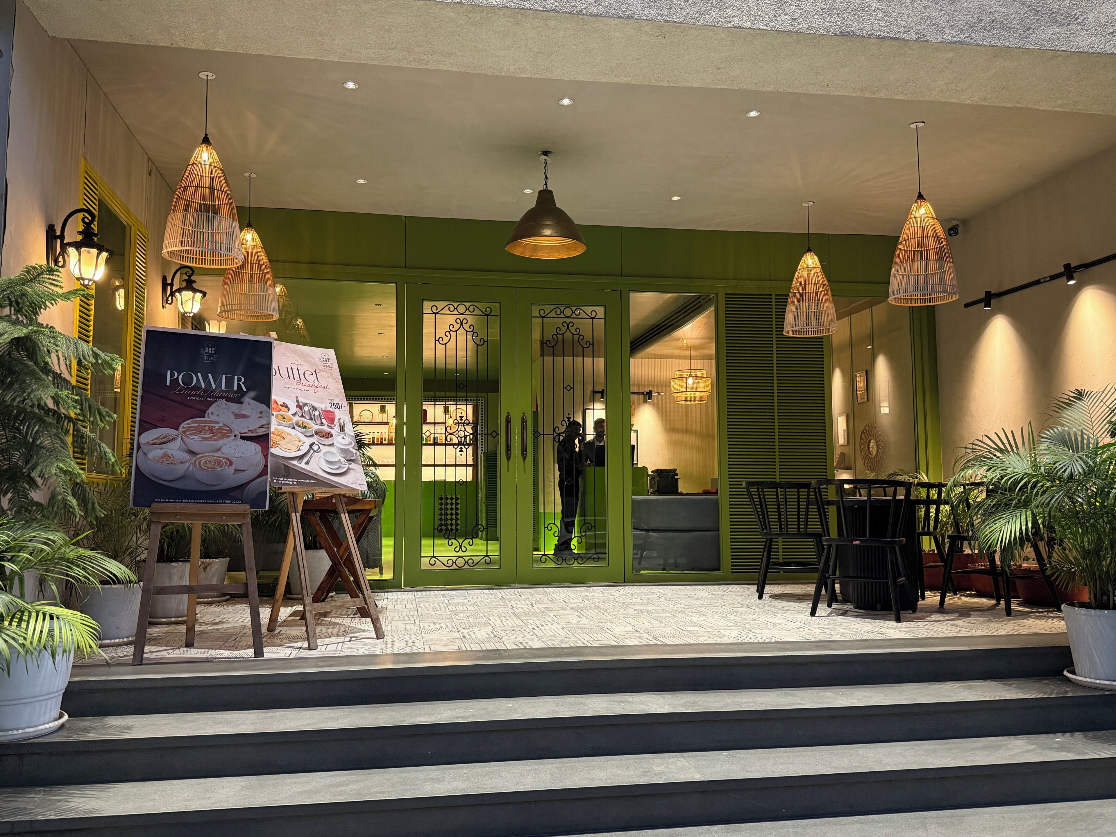 A hotel entrance with a green facade, outdoor seating area, and a buffet advertisement.
