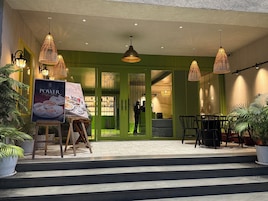 A hotel entrance with a green facade, outdoor seating area, and a buffet advertisement.