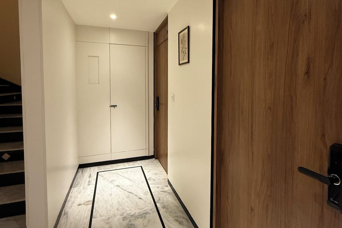 A hallway with a marble floor, wooden door, and a white door at the end.