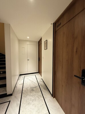A hallway with a marble floor, wooden door, and a white door at the end. - Divik Aparthotel (Bhopal)
