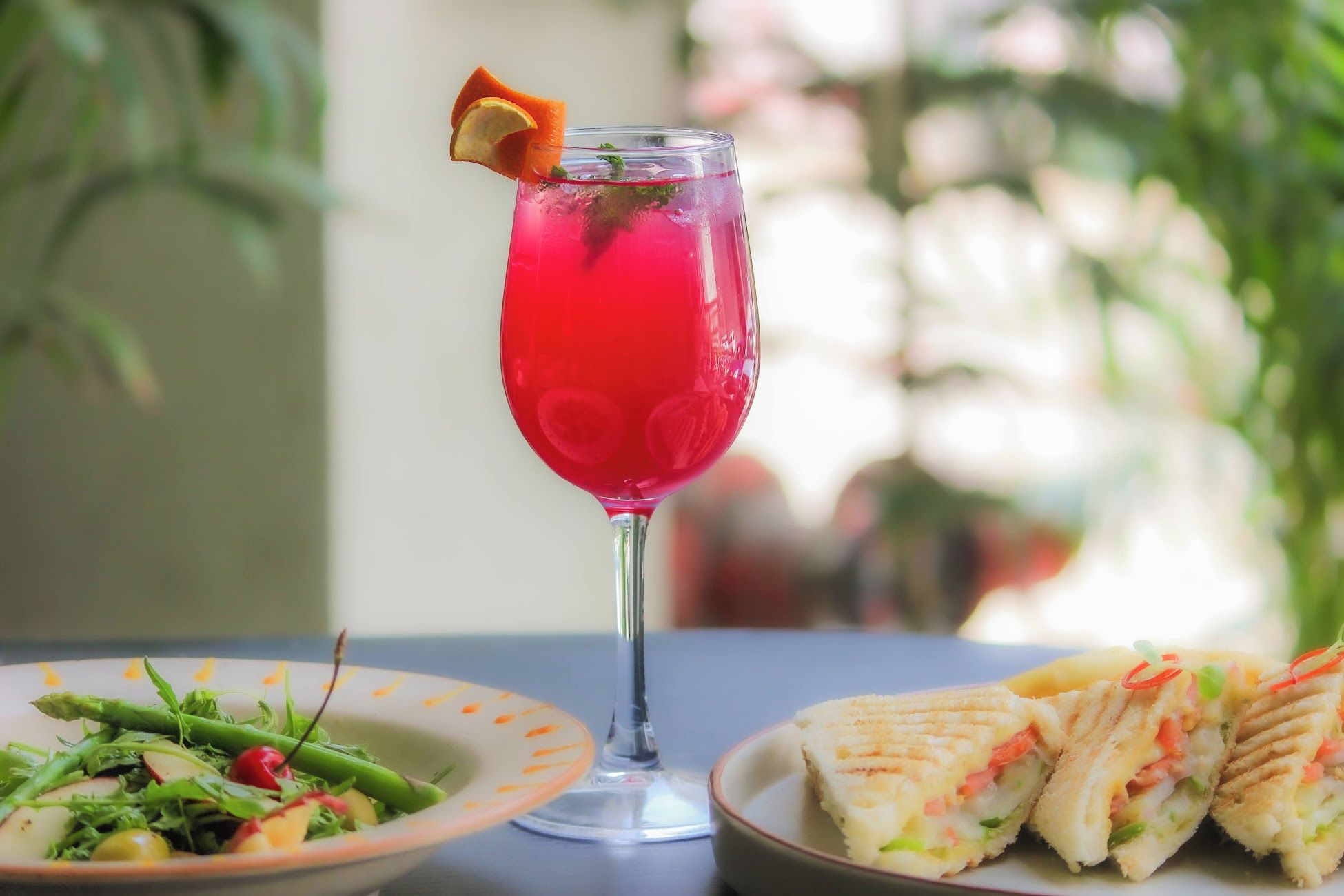 A table with a glass of red beverage, a plate of salad, and a sandwich.
