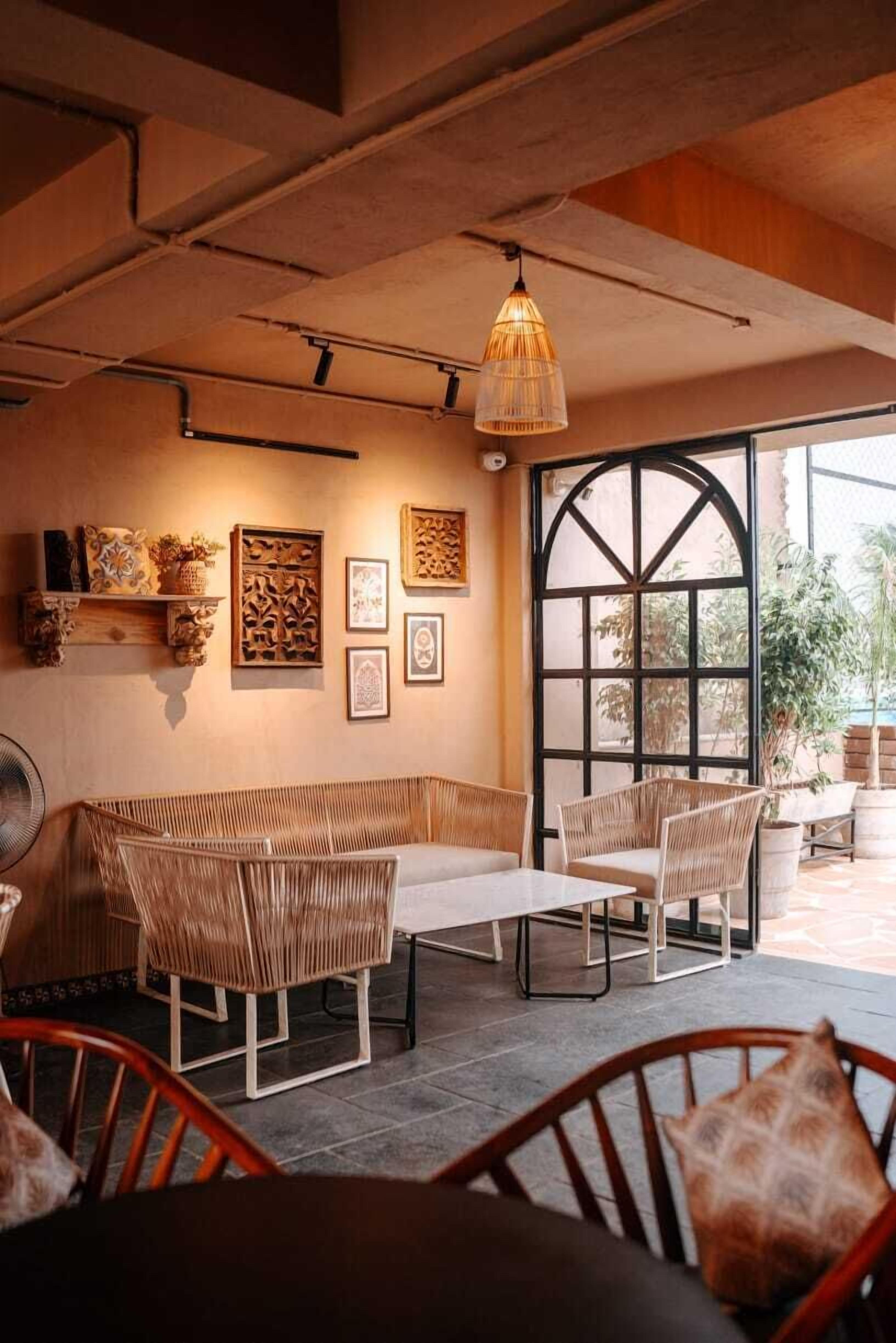A cozy cafe with wicker furniture, a large window, and artwork on the walls.