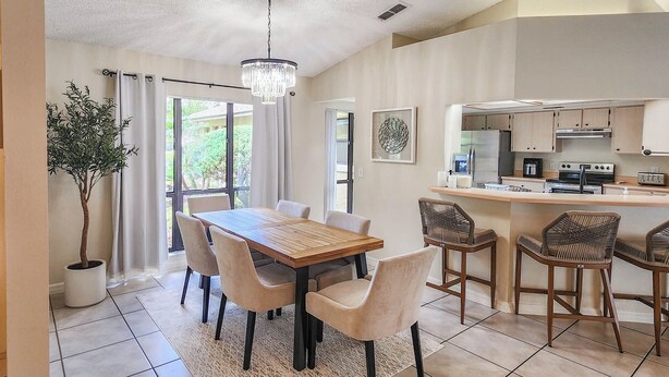 A modern kitchen with stainless steel appliances, a dining area with a wooden table and chairs, and a potted plant. - Solar Heated Pool, Sleeps 10, Peaceful retreat close to shopping and beach! (Palm Coast)