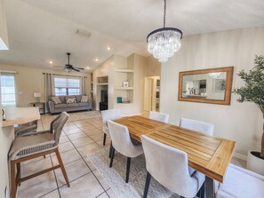Un'elegante sala da pranzo moderna con tavolo e sedie in legno, un lampadario e vista sul soggiorno.