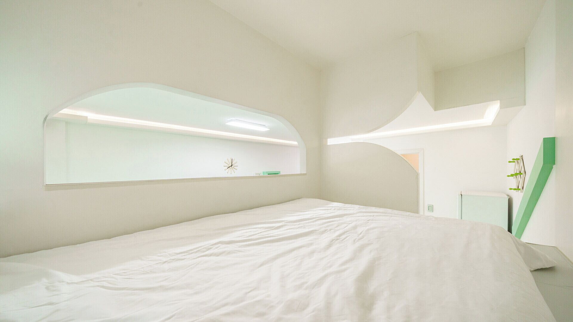 A modern bedroom with a large bed, a wall-mounted mirror, and a green accent wall.