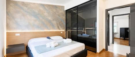 A modern bedroom with a large bed, a nightstand, a wall-mounted light, and a sliding door leading to another room.