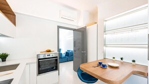 A compact kitchen with a built-in oven, a dining area with a wooden table and blue chairs, and a view of a blue sofa through an open door. - Wonderful House In Portofino With Parking (Portofino)