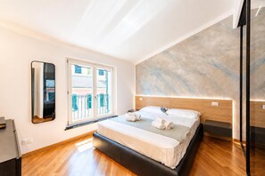 A modern bedroom with a large bed, a mirror, and a view of the outside balcony.