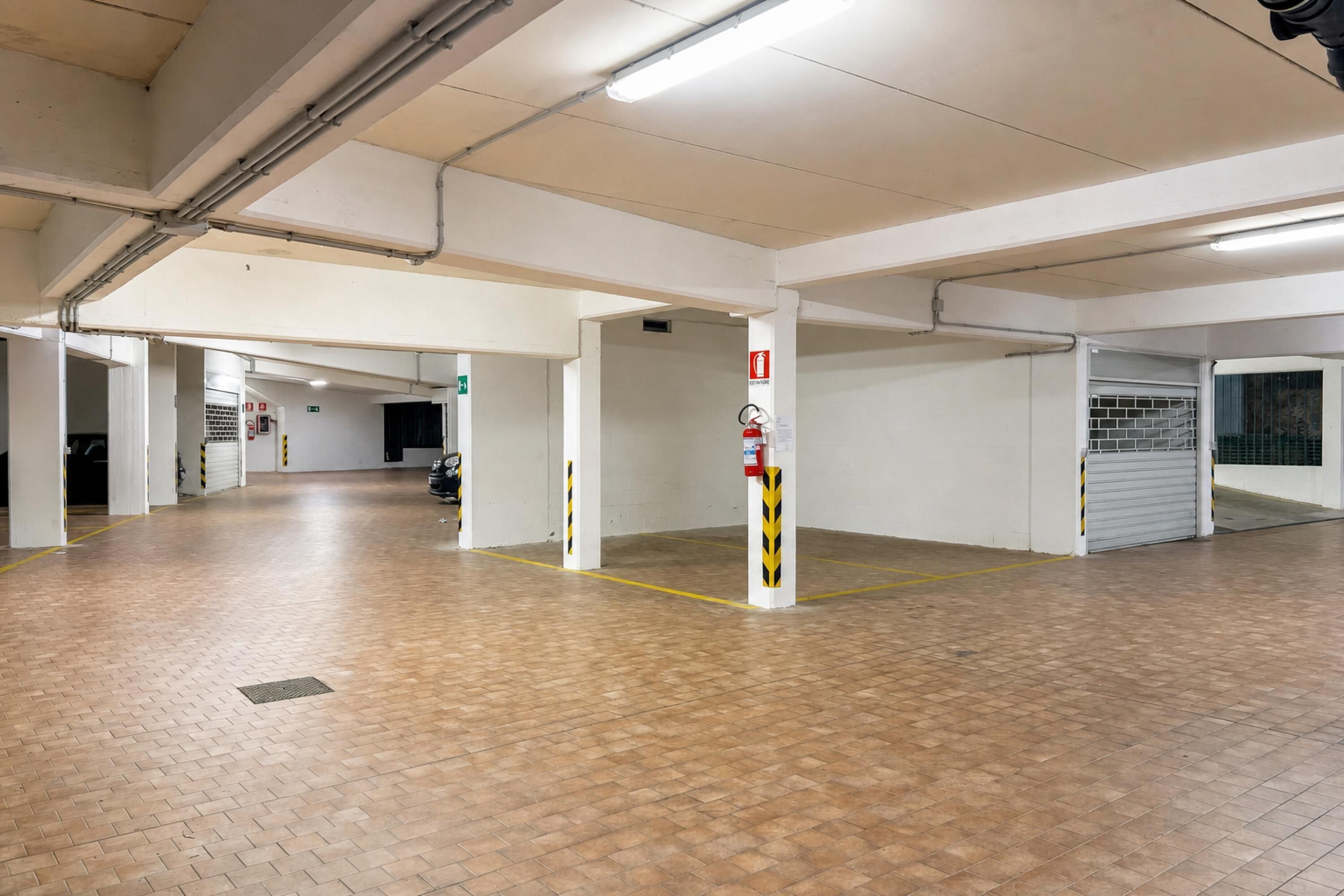 Un vaste espace de stationnement intérieur doté d’un sol carrelé, de murs blancs et d’un extincteur fixé à un pilier.