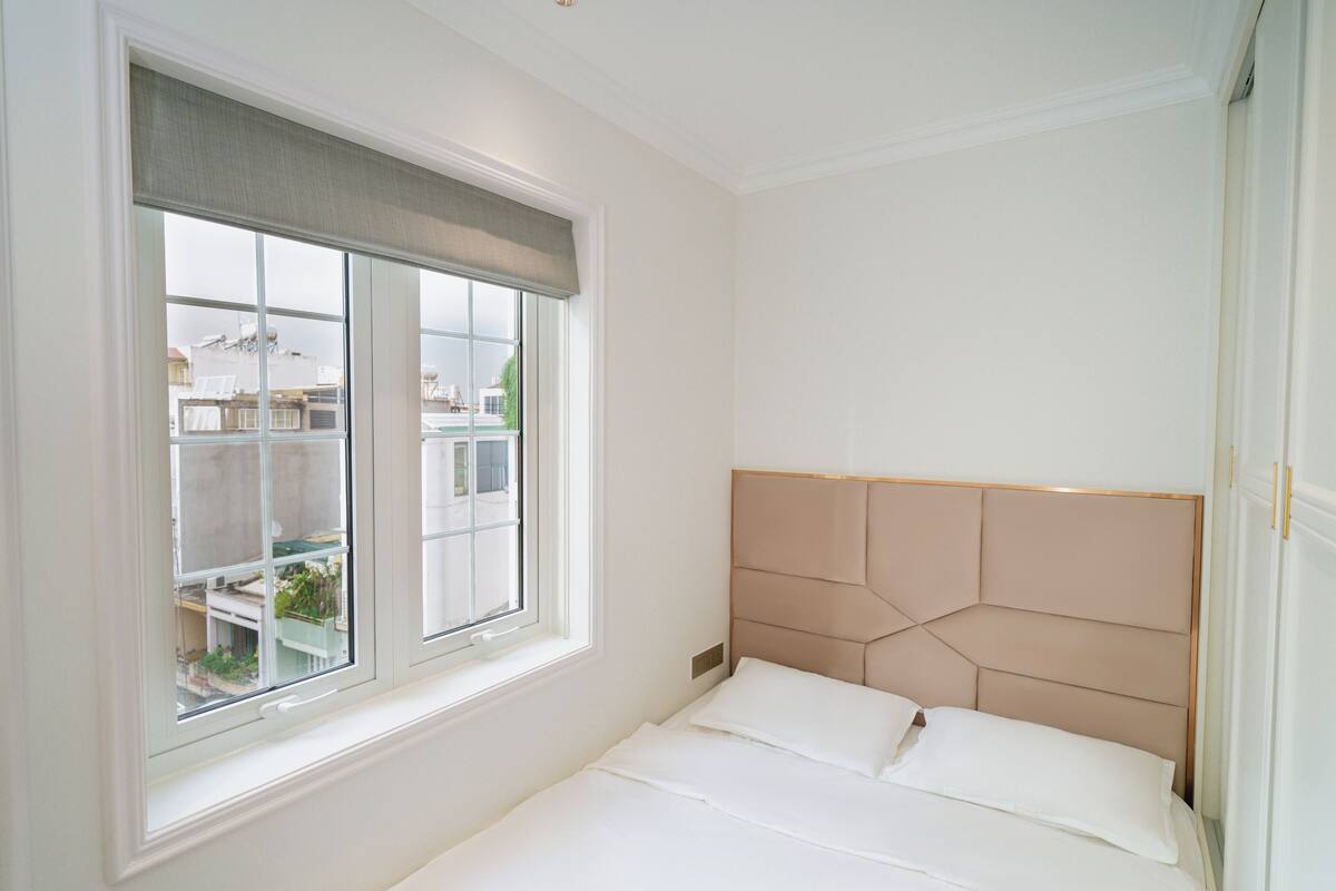 Une chambre avec un lit, une fenêtre donnant sur des immeubles et un mur blanc.