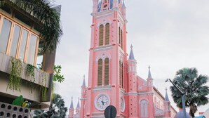 Une église rose dotée d’un clocher, entourée de palmiers et d’une foule de personnes.