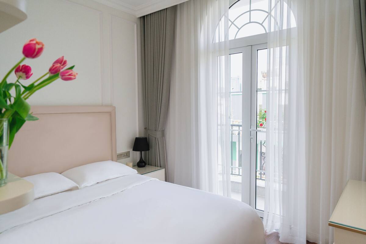 Une chambre d’hôtel avec un lit, une table de chevet, une lampe, un vase de fleurs et une vue sur l’extérieur.