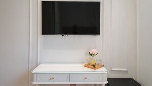 Une table de chevet blanche avec un plateau en verre, un petit vase contenant des fleurs roses et deux verres.