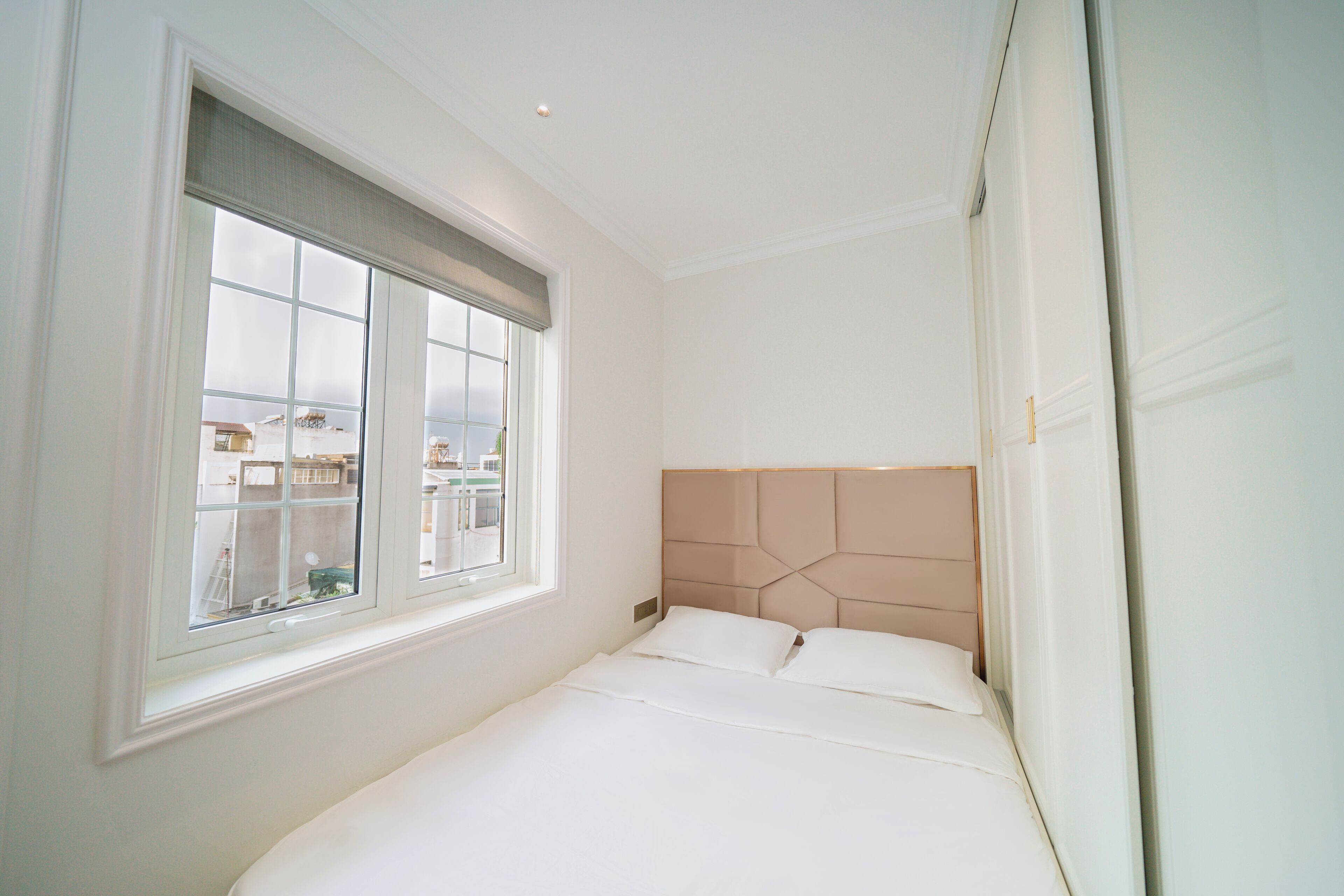 Un dormitorio con un ventanal grande, una cama con ropa blanca y un cabecero moderno.
