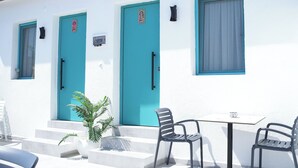 A building with two doors and windows, a small table with chairs, and a potted plant. - Frida Sığacık Butik Otel (Seferihisar)
