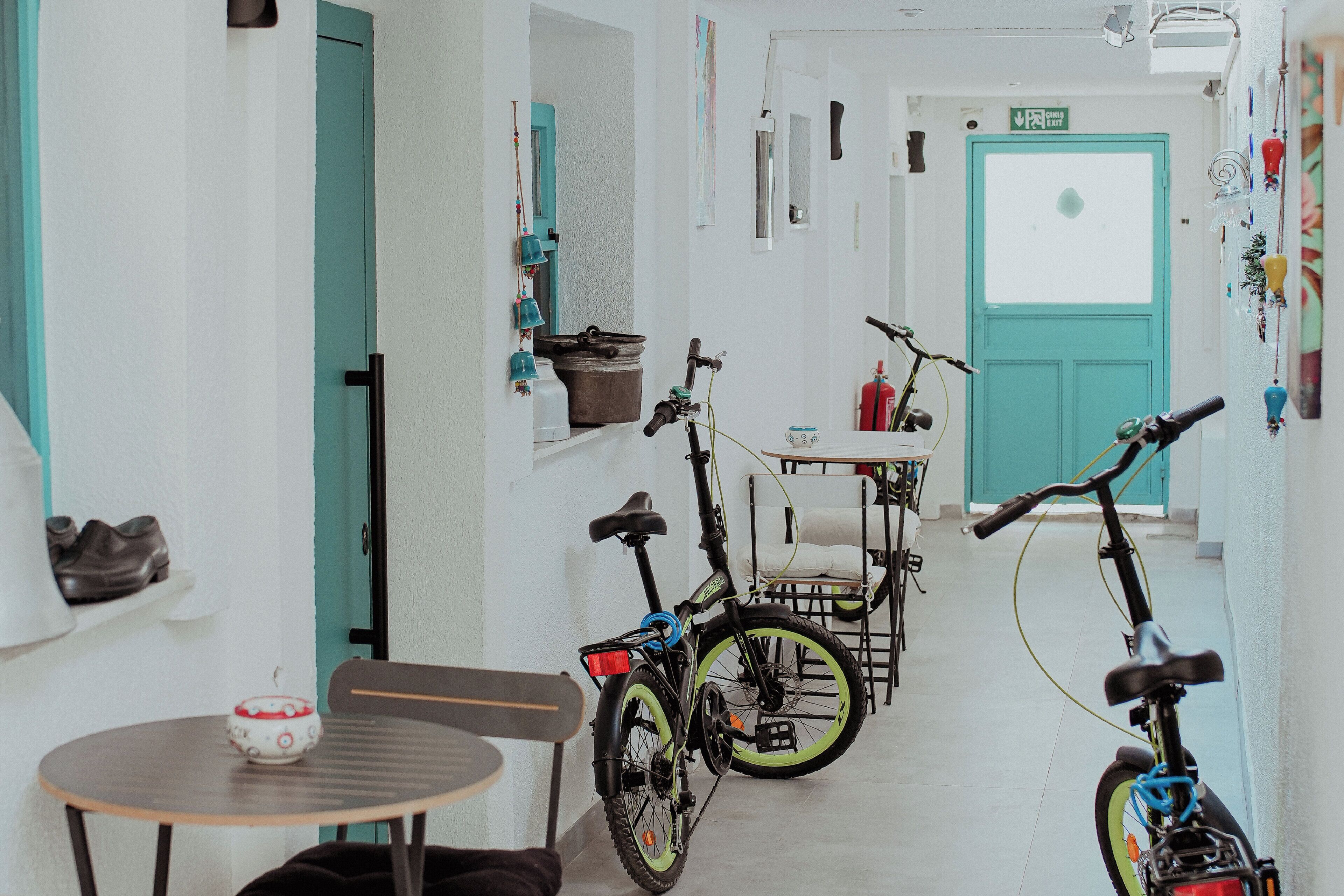 Un pasillo estrecho con bicicletas apoyadas en la pared, una mesa con una silla y una puerta que indica 'EXIT'.