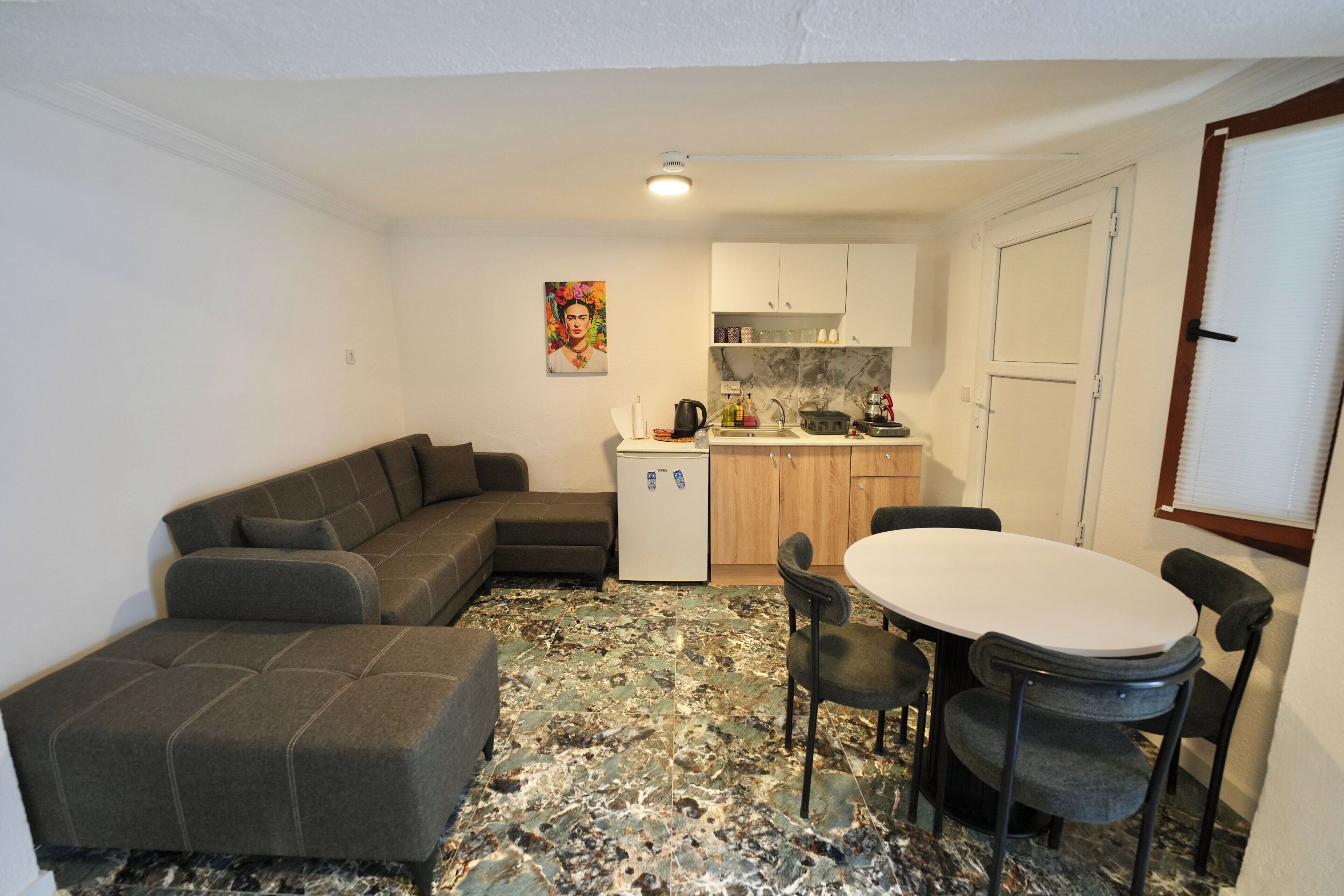 A compact living space with a sofa, a dining table with chairs, a kitchenette, and a refrigerator.