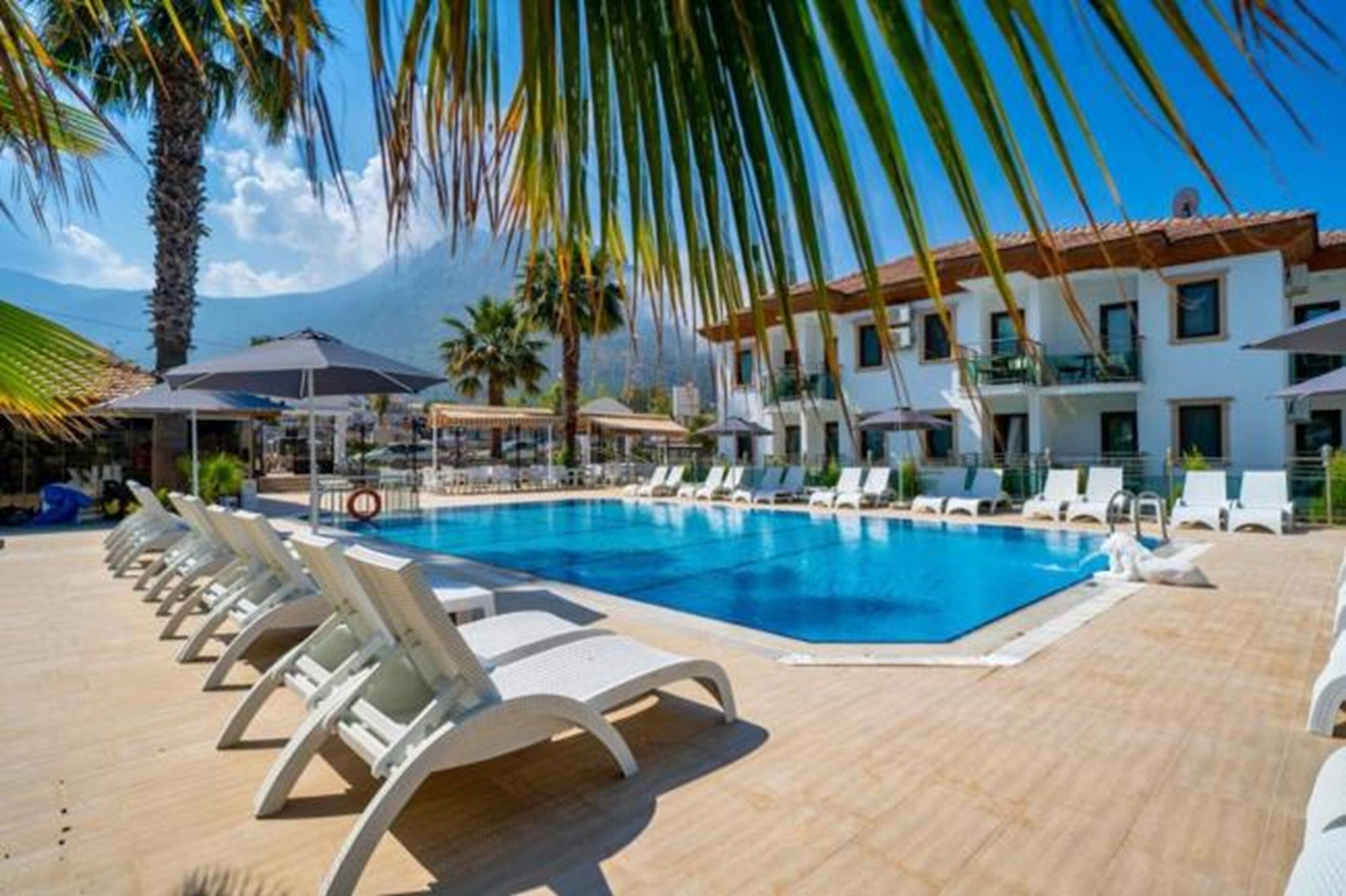 Zona de piscina con sillones de descanso, una piscina y un edificio con balcones.