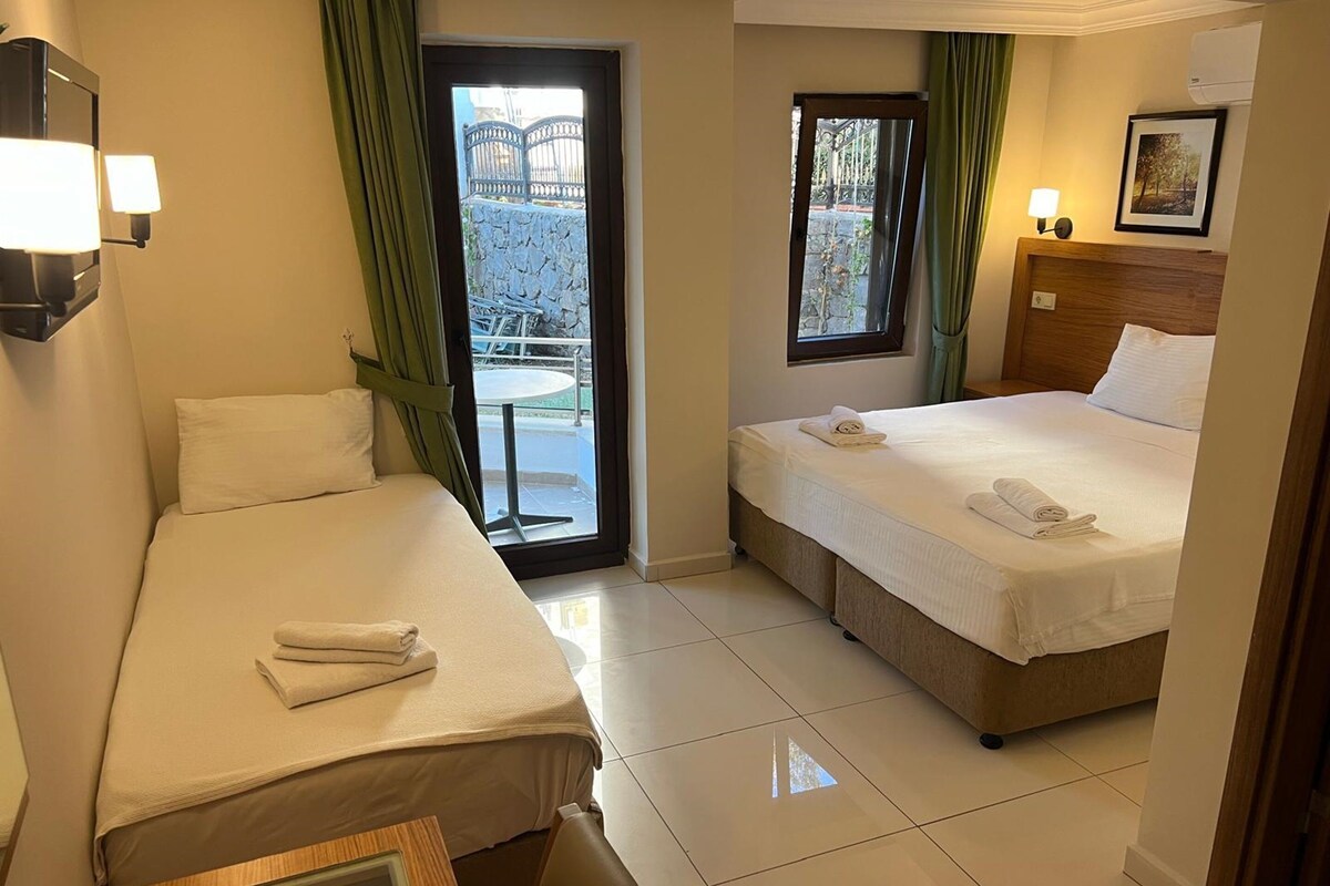 A hotel room with two beds, a small table, and a view of the outside balcony.