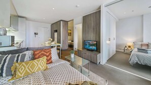 A modern hotel room with a sofa, TV, and a small table. - Perfectly Located 2BR Apartment by Southern Cross (Melbourne)