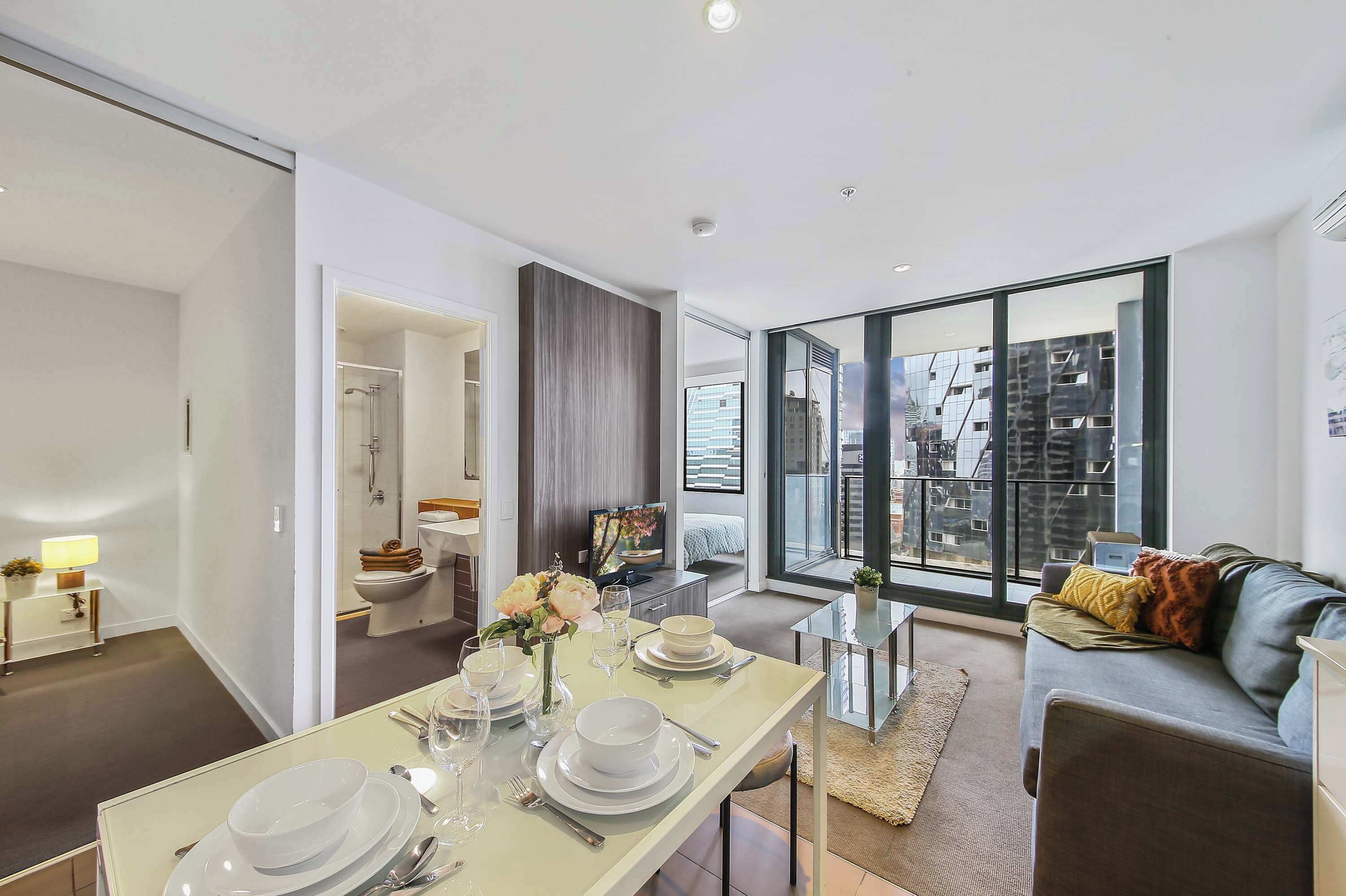 A modern living room with a dining area set for a meal, large windows offering a city view, and a cozy seating area with a sofa.