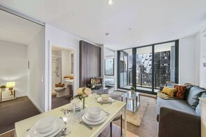 Una sala de estar moderna con comedor listo para una comida, ventanas amplias con vista a la ciudad y una zona de estar acogedora con sofá.