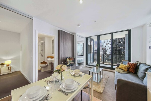 A modern living room with a dining area set for a meal, large windows offering a city view, and a cozy seating area with a sofa.