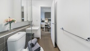 A modern bathroom with a toilet, sink, and mirror. There is a towel rack and a vase with flowers. The bathroom leads to a kitchen area. - Perfectly Located 2BR Apartment by Southern Cross (Melbourne)