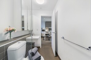A modern bathroom with a toilet, sink, and mirror. There is a towel rack and a vase with flowers. The bathroom leads to a kitchen area.
