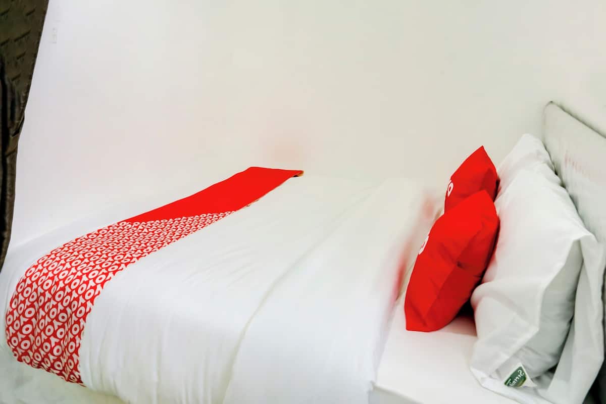 Uma cama com colcha branca e vermelha estampada, um travesseiro vermelho e um travesseiro branco em cabeceira branca.