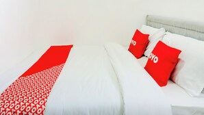Una cama con ropa de cama blanca y almohadas rojas, un corredor con estampado rojo y blanco, y un cabecero de color claro.