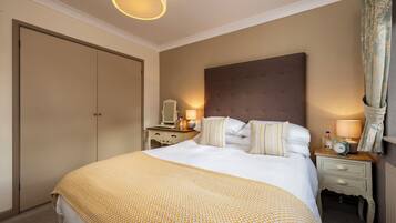 A hotel room with a large bed, bedside tables, a nightstand, a mirror, and a lamp.