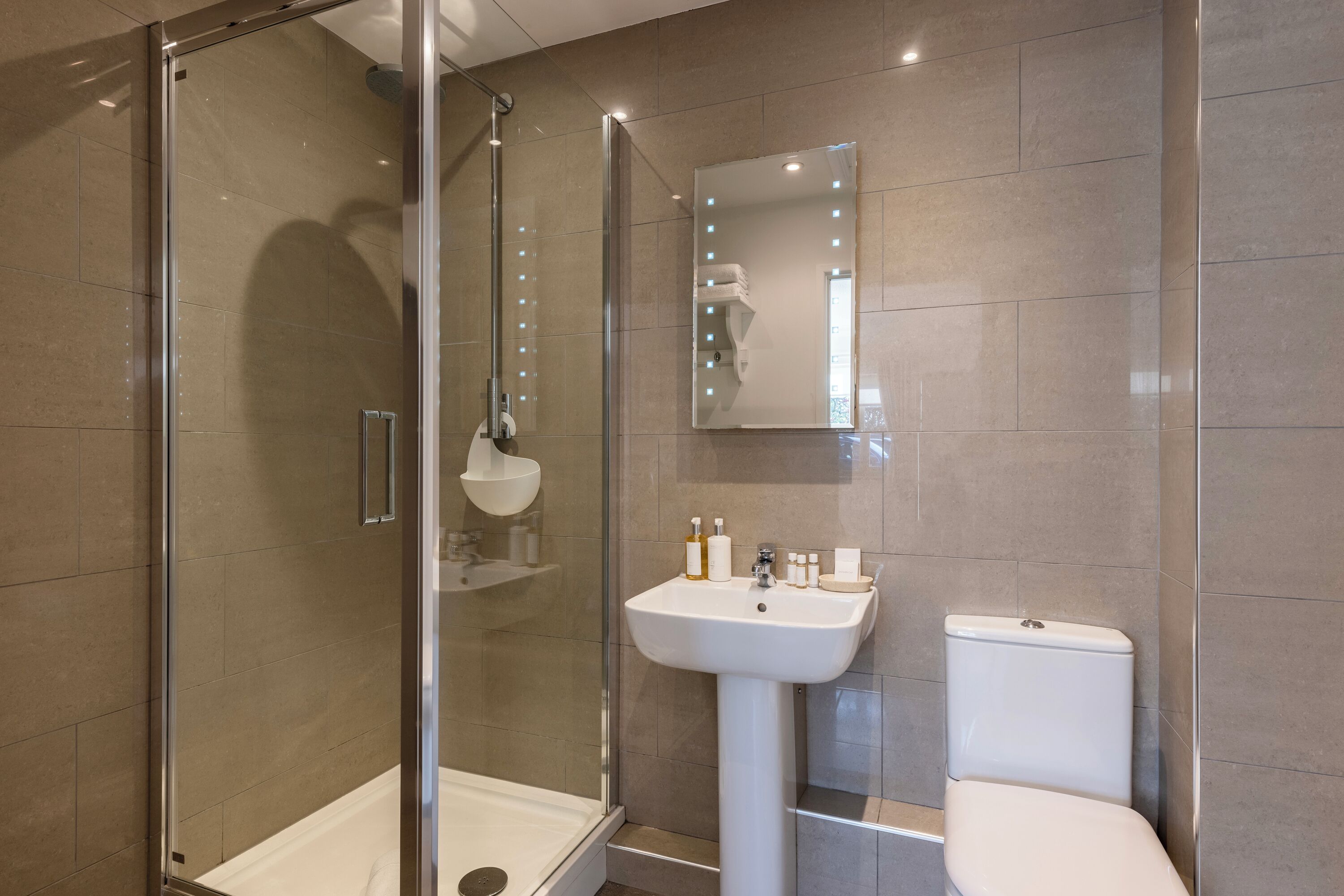 Un baño moderno con ducha envuelta en vidrio, lavamanos pedestal y retrete.