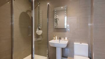 Un baño moderno con ducha envuelta en vidrio, lavamanos pedestal y retrete.