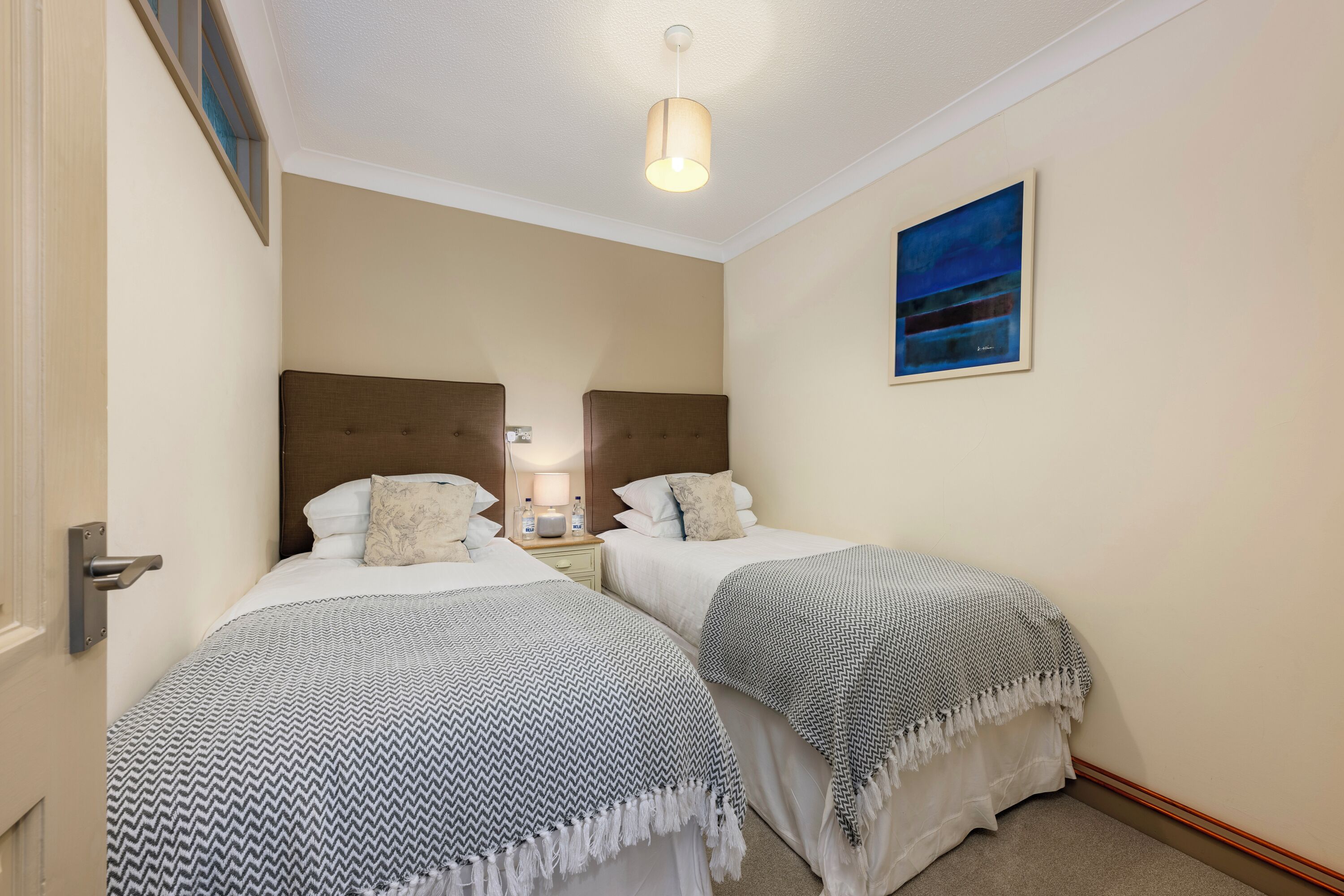 Ein Hotelzimmer mit zwei Betten, jeweils mit gemusterten Bettdecken und Kissen. An der Wand hängt ein Gemälde und es gibt eine Deckenleuchte.