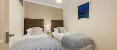 Ein Hotelzimmer mit zwei Betten, jeweils mit gemusterten Bettdecken und Kissen. An der Wand hängt ein Gemälde und es gibt eine Deckenleuchte.