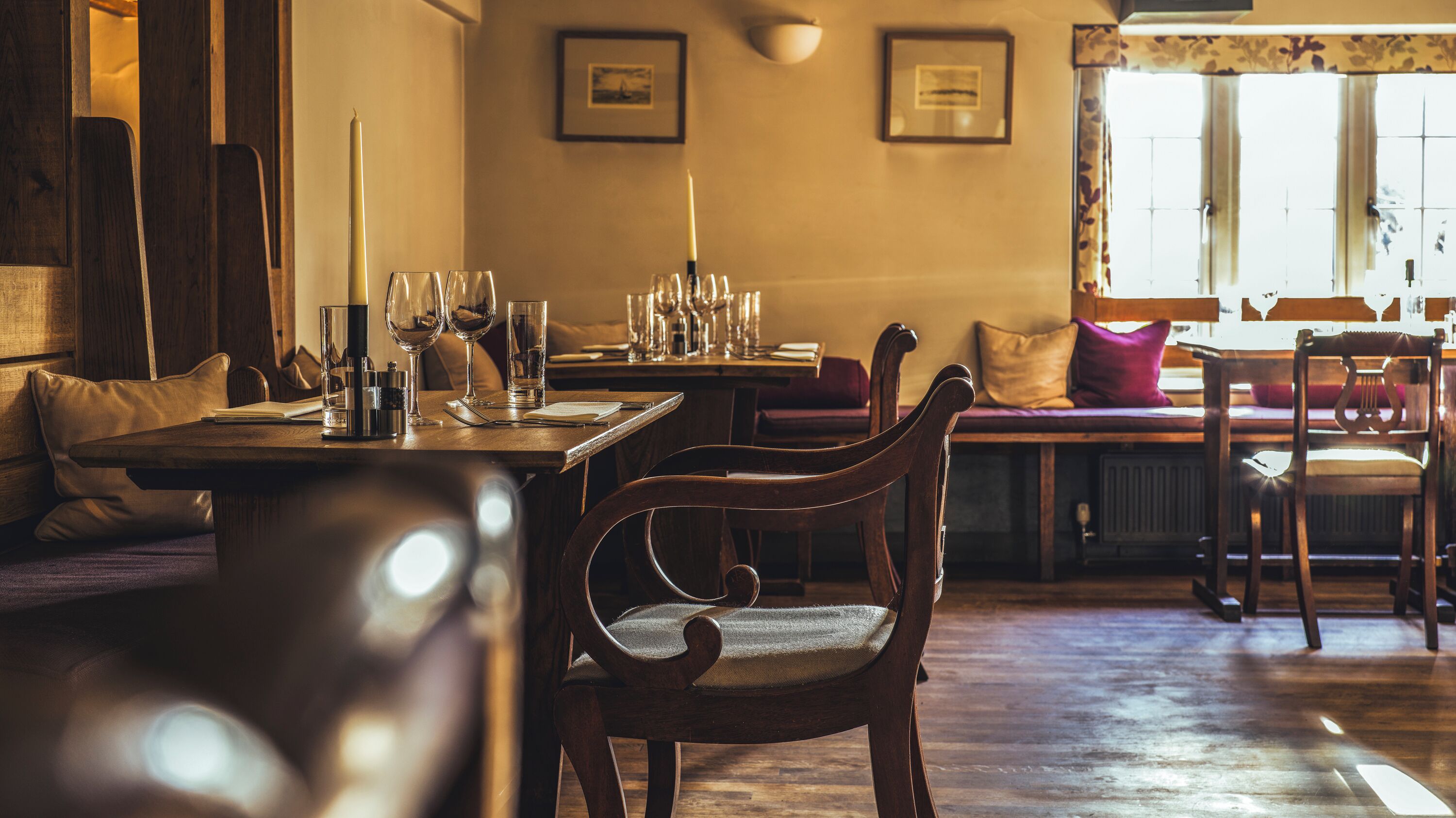 Un comedor acogedor con muebles de madera, una mesa dispuesta con vasos y una vela, y una ventana con cortinas.