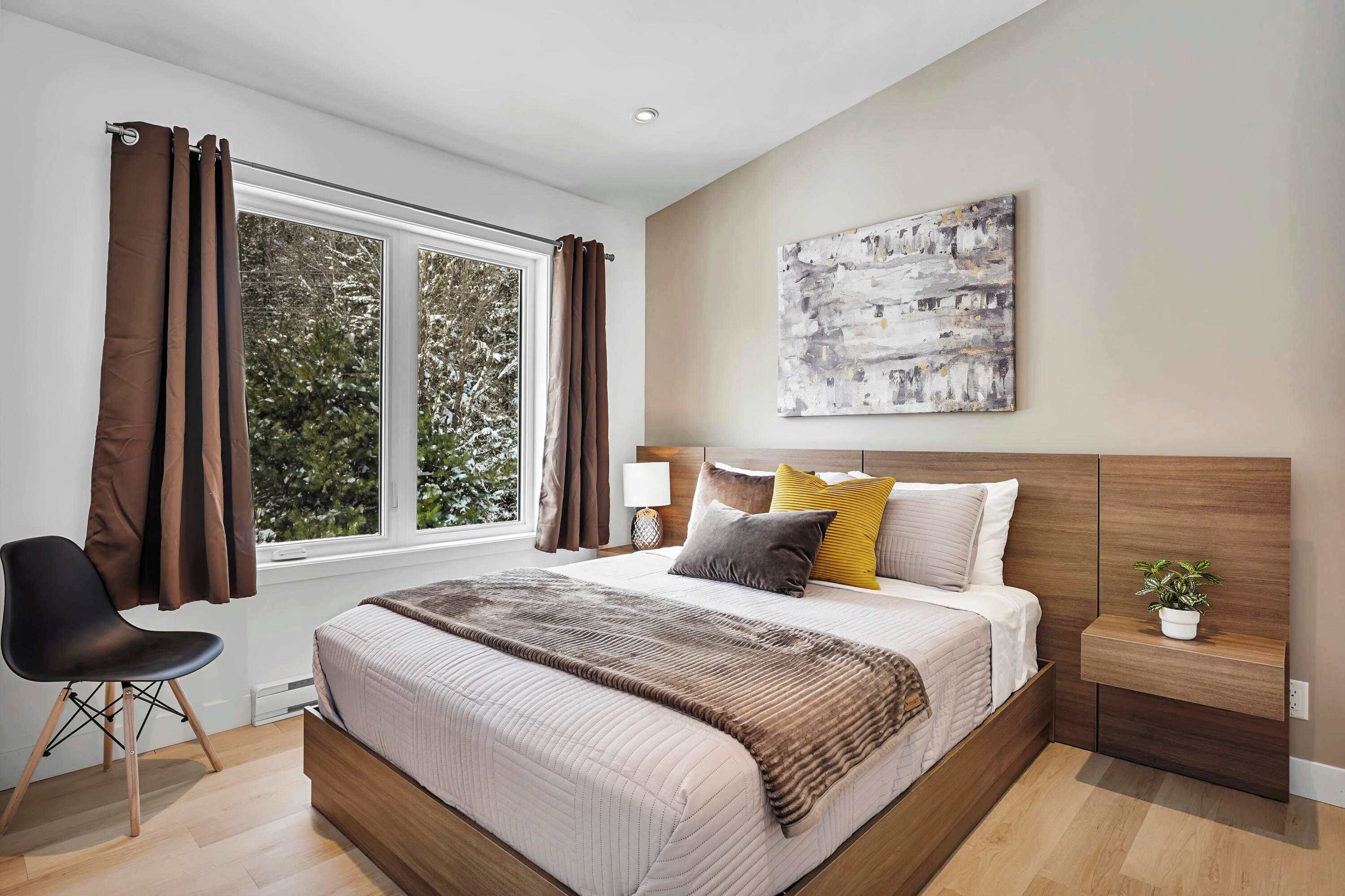 A modern bedroom with a large bed, a bedside table with a lamp, a chair, and a window with curtains.