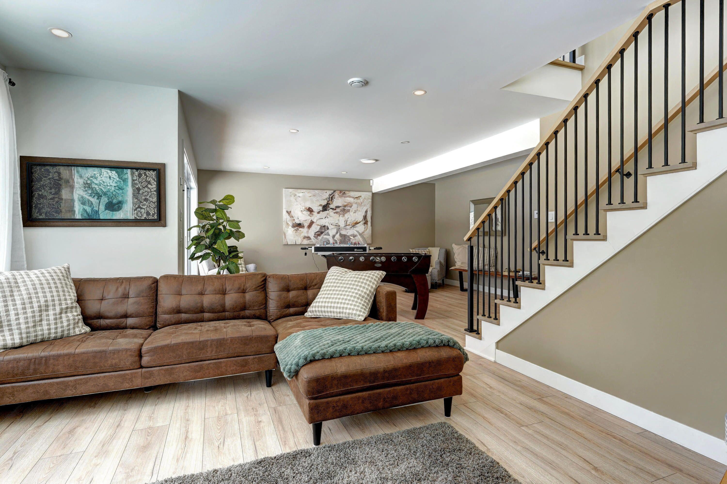 A living room with a brown leather sectional sofa, a green throw blanket, a wooden coffee table, and a foosball table.