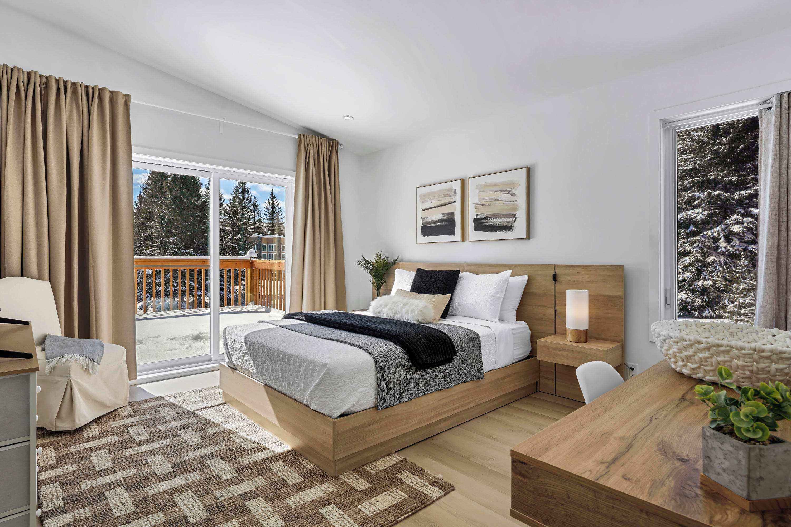 Quarto moderno com cama grande, escrivaninha de madeira e varanda com vista para árvores e deck de madeira.