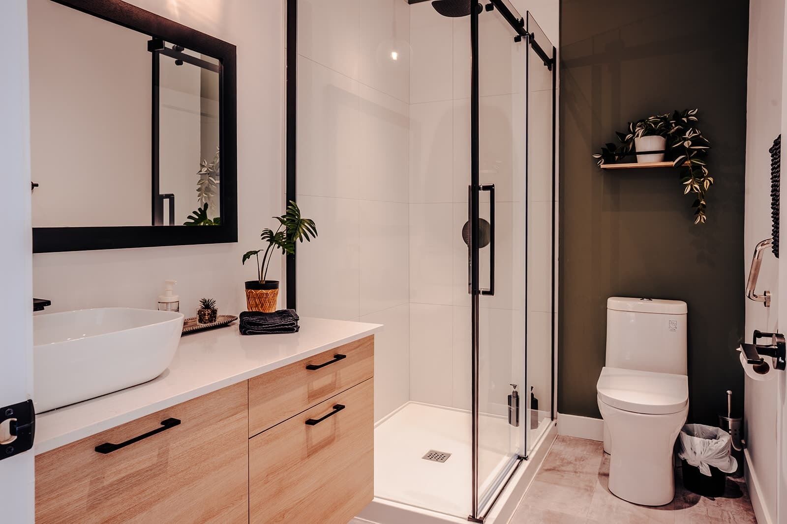 Een moderne badkamer met een glazen douchecabine, een witte wastafel en een toilet.