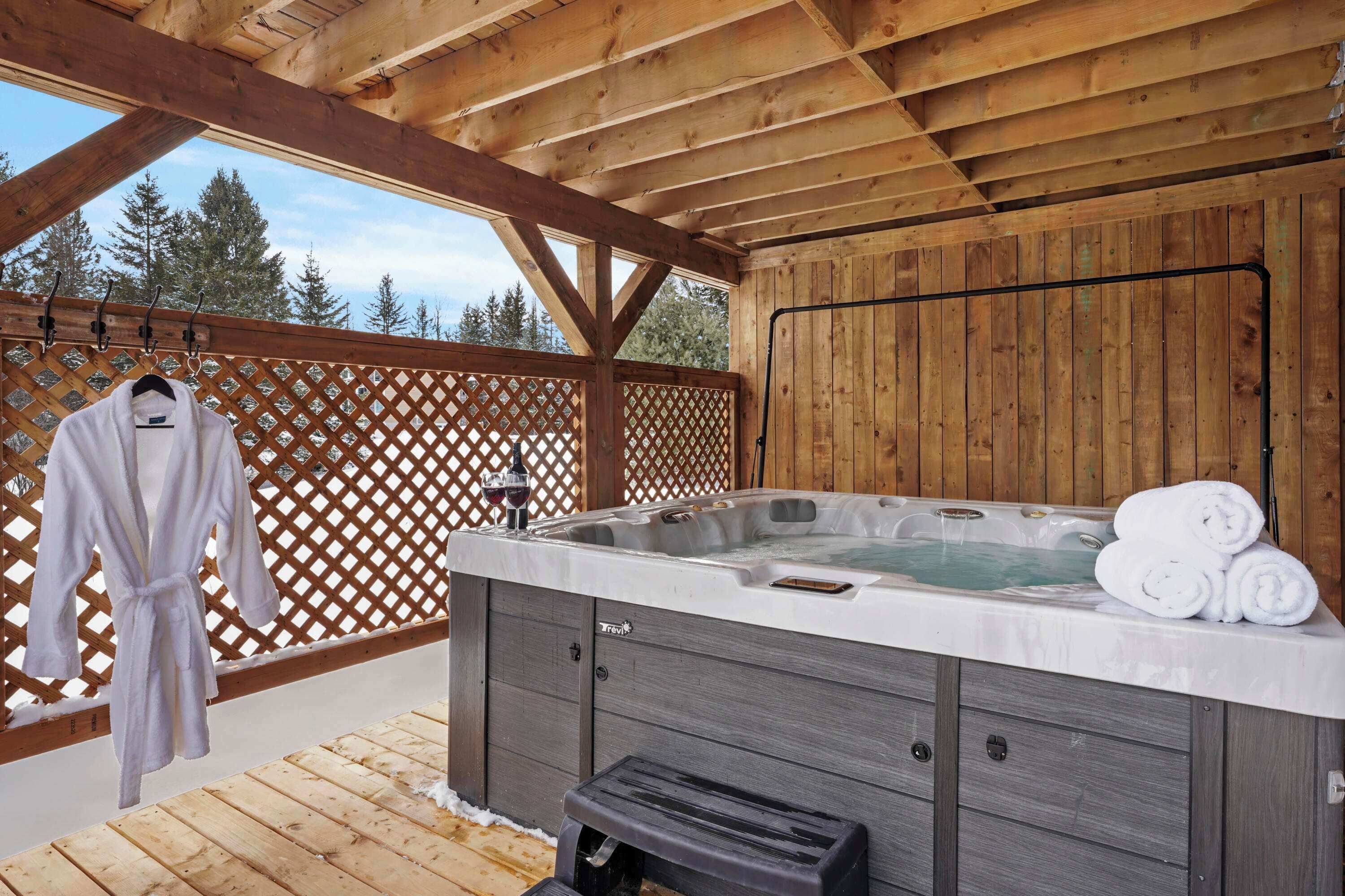 A wooden deck with a hot tub, a wooden lattice fence, and a white robe hanging on a rack.