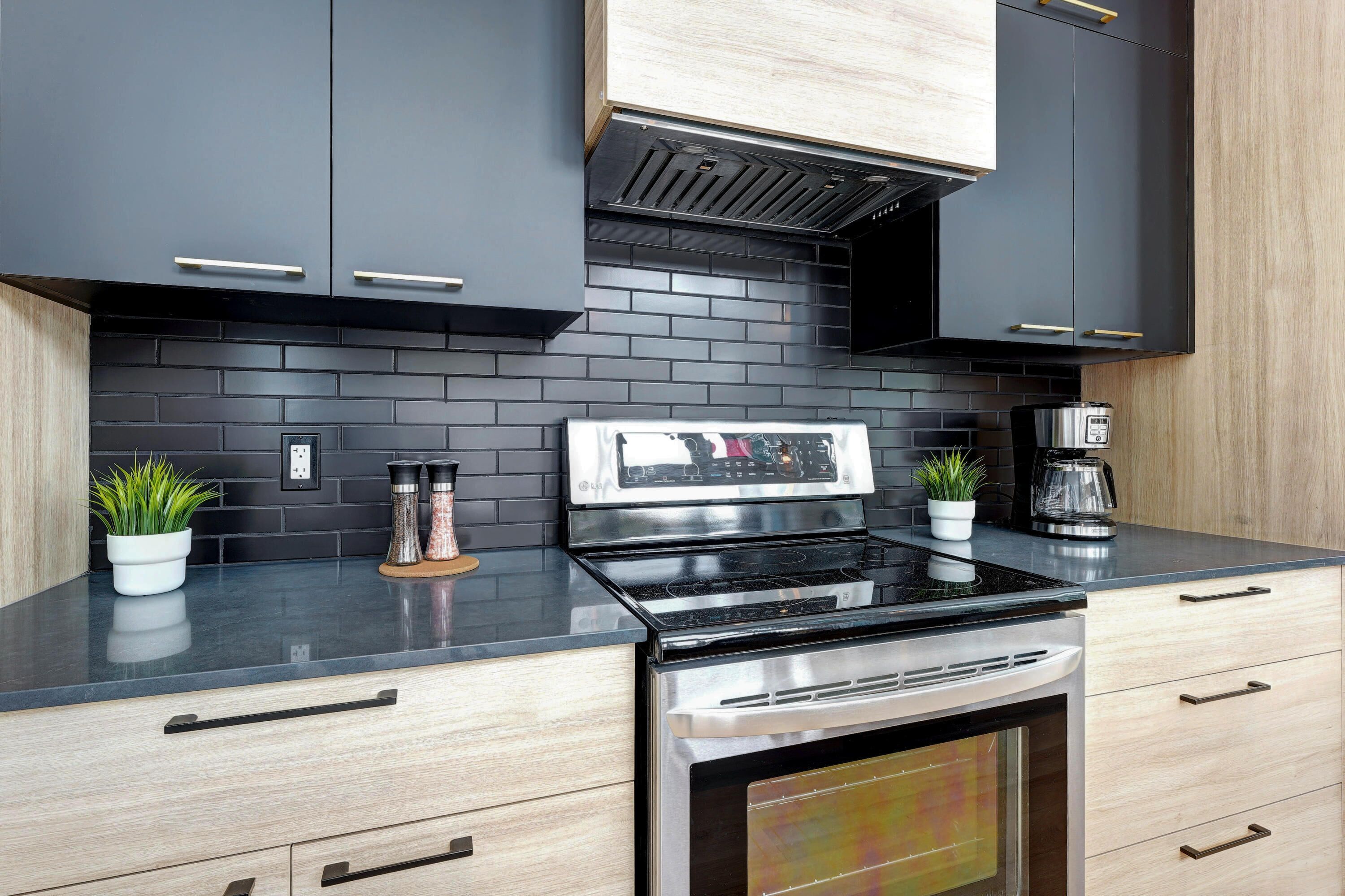 Een moderne keuken met een zwart betegelde spatwand, roestvrijstalen apparatuur en houten kastjes.