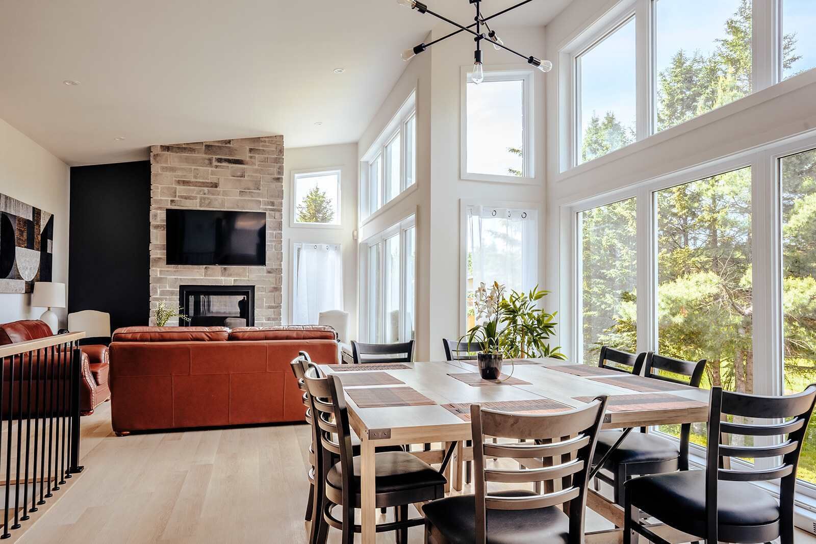 A modern living room with a fireplace, a dining area with a large table and chairs, and a TV mounted on the wall.